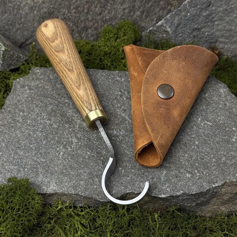 A hand-forged carbon steel 52100 tool, suitable for beginners, includes a hook knife with a leather case, a spoon, a bowl and a cup carving